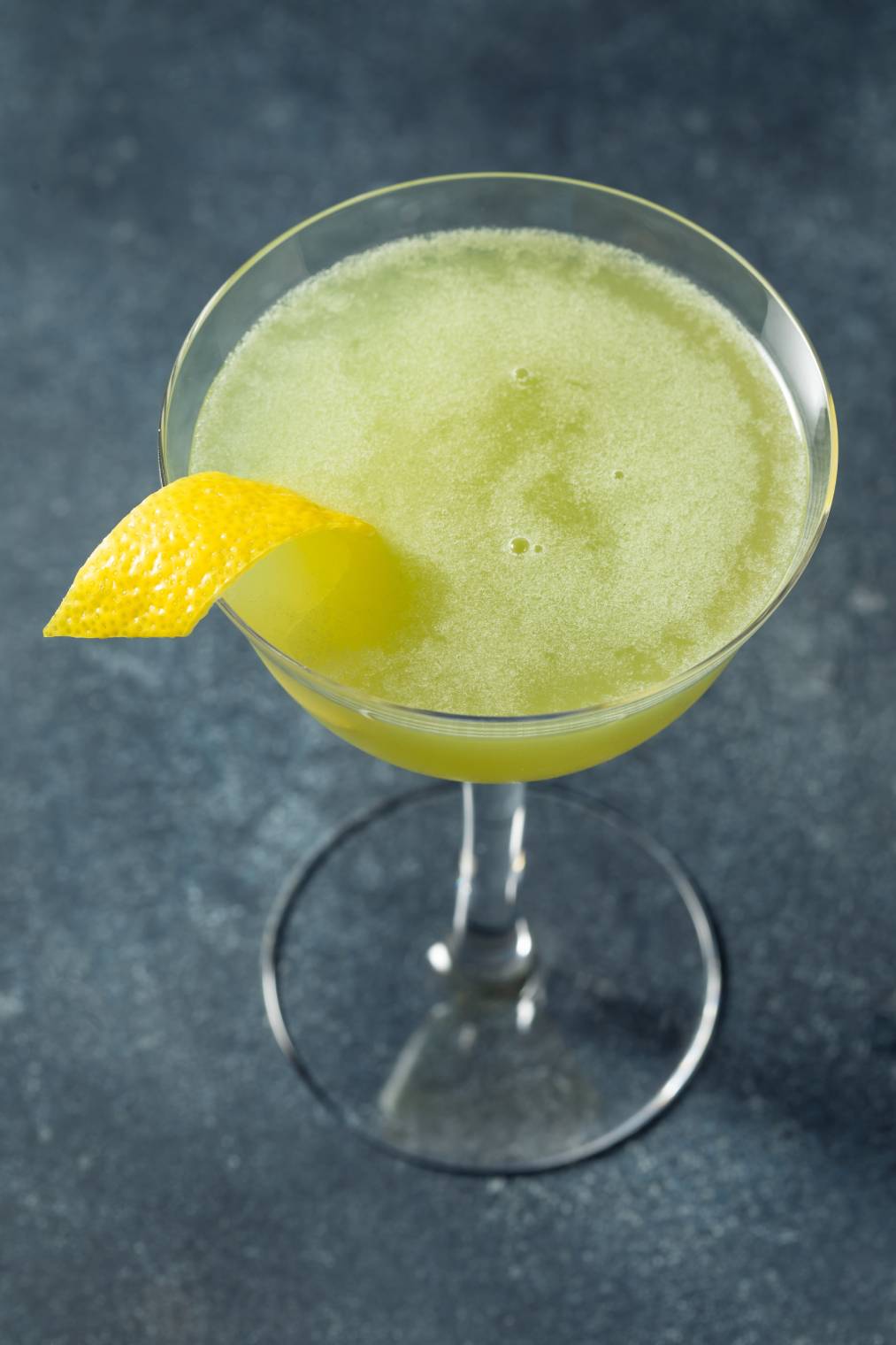 A green cocktail with a lemon wedge on top.
